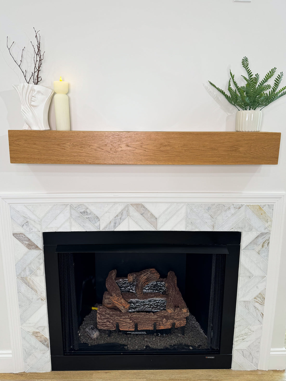 Fireplace with wooden mantel, candles, and plants against a white wall